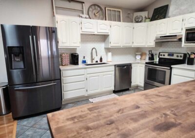 Dark Gray Refrigerator, sink, oven, white kitchen counters and cabinets and solid wood finished counter