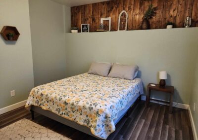 bedroom with bed and side table, bright patterned sheets, wood floors, lamp on side table, and wood decor